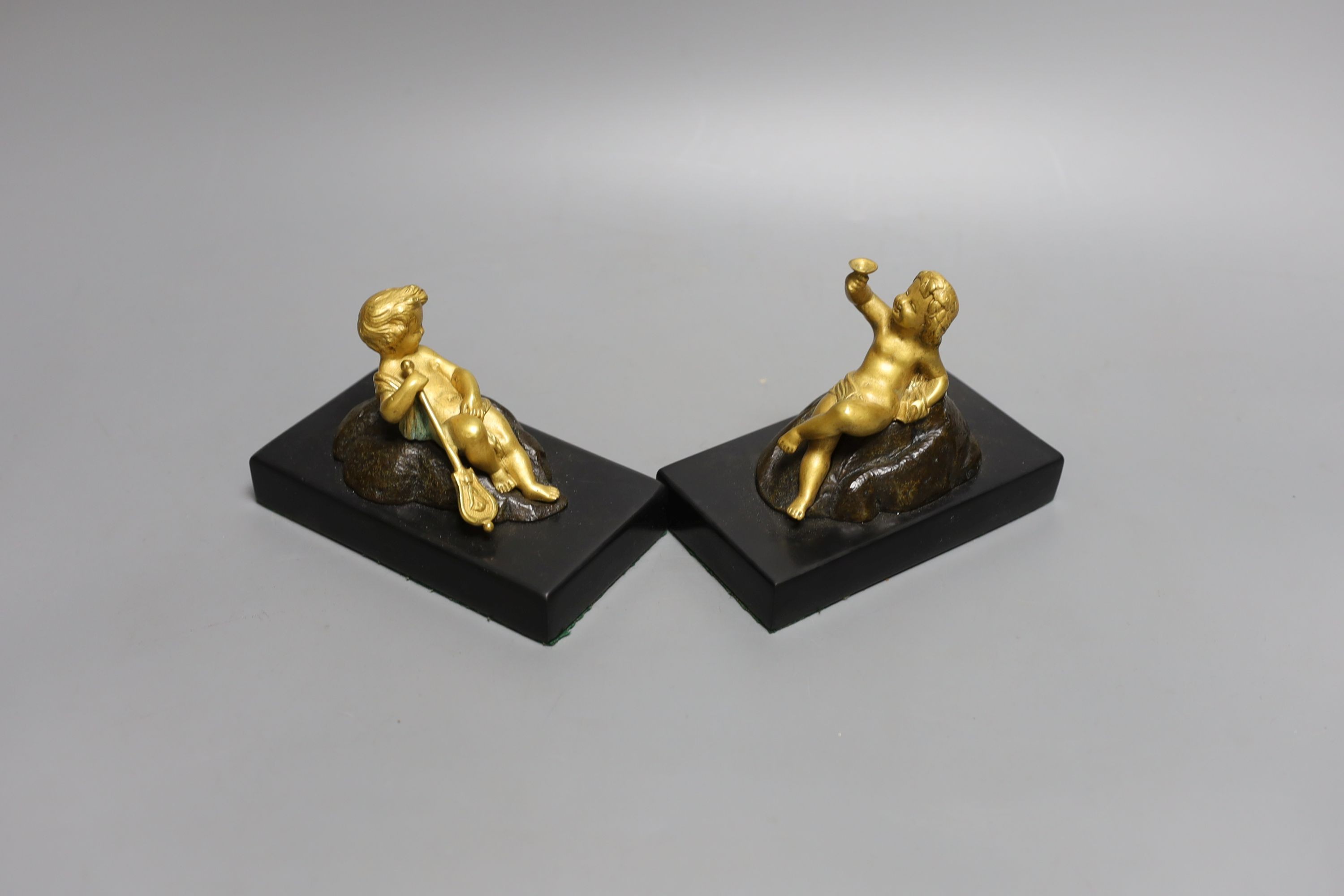 A pair of ormolu putto paperweights on black marble bases, 13 cms wide.